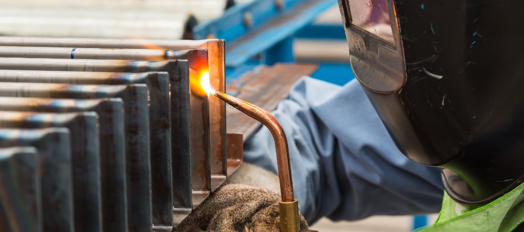 Welder in protective gear using a torch to weld metal pieces in an industrial setting. Bright flame against metal, indicating precision and focus.
